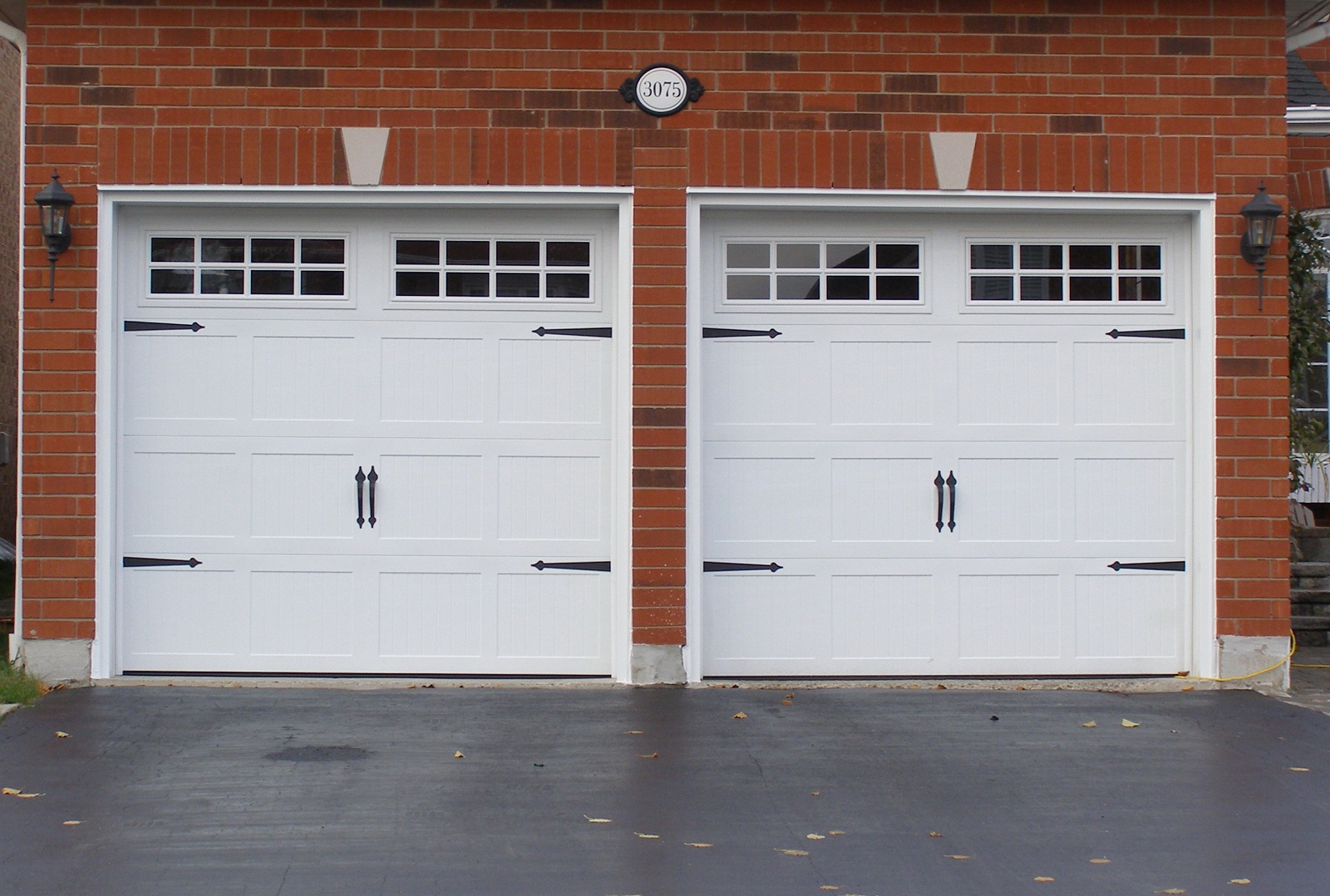 White carriage-style garage doors with decorative hardware on a brick home